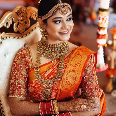 A classic South Indian bride in all her glory. This look features a stunning red and orange Kanjeevaram silk saree, paired with a heavily embroidered blouse and traditional temple jewelry for the main wedding ceremony.