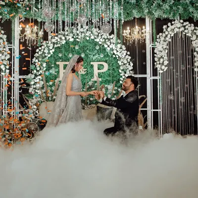 A fairytale proposal moment during the engagement, with the groom on one knee, surrounded by theatrical smoke and a beautiful floral backdrop.