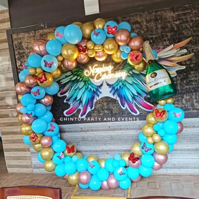 A custom balloon ring decoration for a Naming Ceremony. This setup features a 'Naming Ceremony' neon sign with angel wings, surrounded by a ring of blue, gold, and rose gold balloons with butterfly accents.