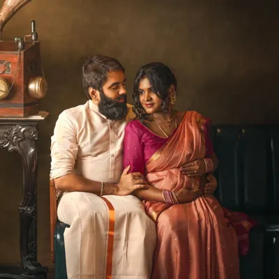 A couple shares a look of love in a vintage-inspired studio setting, complete with a gramophone and traditional Indian attire. This fine art maternity portrait is rich in color and emotion.