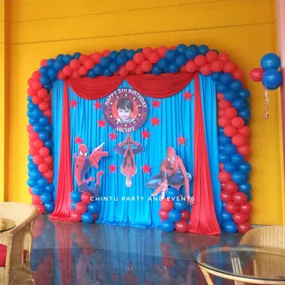 A classic Spiderman theme stage for a 5th birthday, featuring a vibrant red and blue balloon arch, character cutouts, and a personalized backdrop.