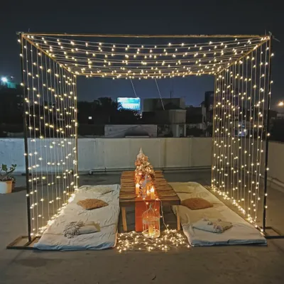 A magical rooftop dining setup under a canopy of fairy lights. This romantic arrangement includes low seating with mattresses and cushions, perfect for a quiet birthday evening under the stars.