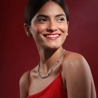 A radiant smile complemented by a delicate diamond and sapphire necklace. This lifestyle jewelry shot against a rich red background focuses on how the piece looks and feels when worn.