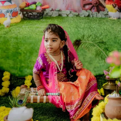 A beautiful portrait of a little girl dressed as Radha for a Janmashtami celebration. The vibrant set, complete with marigolds and a pot of butter, brings the festival to life.