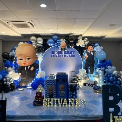 A full stage setup for a Boss Baby theme party, complete with character cutouts, a custom circular backdrop, and themed pedestal tables for the cake.