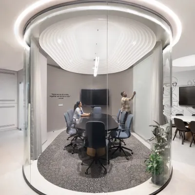 This unique cylindrical glass meeting pod is a centerpiece of the office. It offers acoustic privacy for meetings while its transparency maintains the open-plan feel. The sculpted ceiling and halo light add a futuristic touch.