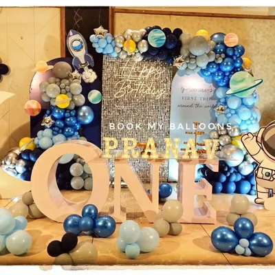 A spectacular space-themed first birthday party, featuring a large moon prop, rocket cutouts, an astronaut figure, and a stunning balloon galaxy arch.