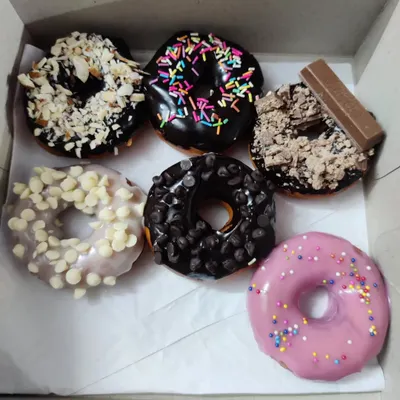 This assorted donut box shows the variety of toppings you can choose from. It features white chocolate chip, KitKat crumble, almond crunch, dark chocolate chip, and classic rainbow sprinkles.
