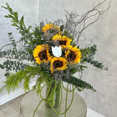 An emblem of happiness, the glorious Sunflower. This arrangement celebrates the flower that inspired Van Gogh, pairing its cheerful yellow faces with wild, woody stems and lush foliage for a rustic yet joyful look.