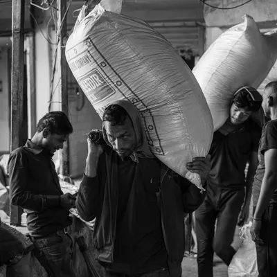 A laborer carries a heavy sack through the crowded lanes of Khari Baoli spice market. This black and white documentary shot highlights the grit and hard work that defines daily life here.