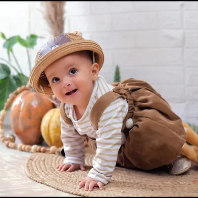 An adorable sitter session with an autumn theme. This baby is dressed in cute overalls and a hat, crawling on a mat surrounded by pumpkins.