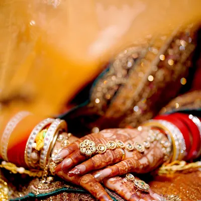 A close-up on the bride's hands, showcasing the intricate henna design, the traditional 'chooda' bangles, and the beautiful hand jewelry.