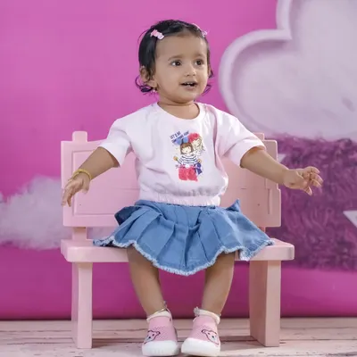 A happy little girl on a pink bench against a matching pink backdrop. Our studio is equipped with a variety of colorful backgrounds.