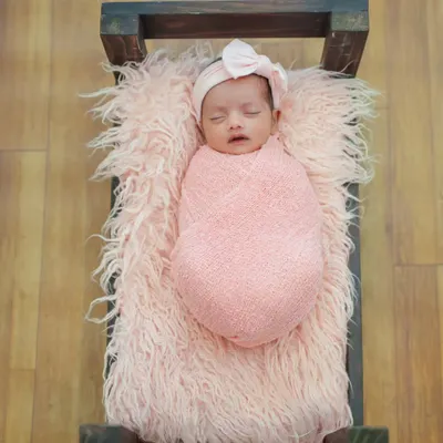 An overhead shot of a newborn sleeping peacefully in a rustic prop bed. The soft pink fur and matching swaddle create a cozy and coordinated look for this studio baby shoot.