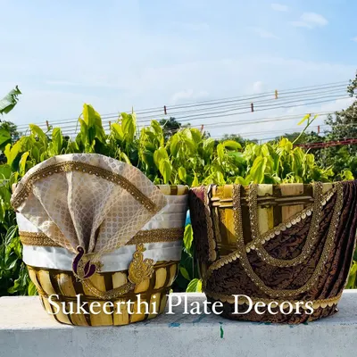 A pair of decorated Uppukudai for an engagement. The 'groom' basket features a turban, and the 'bride' basket is draped in a miniature saree.