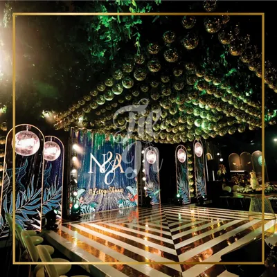 The heart of the celebration was this striking dance floor with a geometric mirror pattern, set against a custom LED screen and flanked by panels with tropical prints. The ceiling is a dense canopy of foliage and gold mirror balls, designed to immerse guests in a wild, glamorous wonderland.