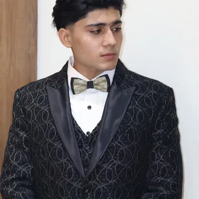 A closer look at a custom-designed three-piece tuxedo. The jacket features a subtle, intricate pattern, paired with a classic waistcoat and a sparkling bow tie for a touch of modern elegance.