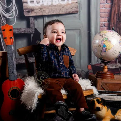 A burst of pure happiness in our rustic cowboy themed set. This little guy's joyful laugh is infectious, surrounded by props like a guitar, globe, and a stuffed dog.