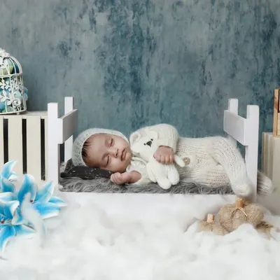 A newborn sleeps peacefully in a miniature bed, dressed in a cozy knit outfit. Our two-month milestone sessions capture how much they've grown in just a few weeks.