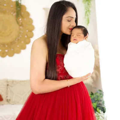 A mother's love captured in a single frame. This portrait of a new mom in a striking red dress holding her sleeping newborn is full of warmth and tenderness.
