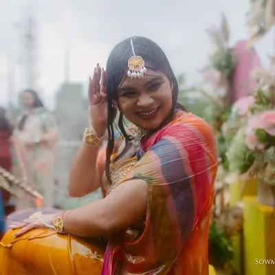 The pure fun of a Haldi ceremony. This bride is all smiles as she gets drenched in water, her colorful saree adding to the festive mood.