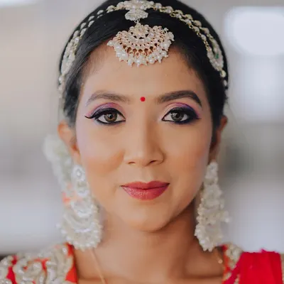 A striking beauty portrait. The focus is entirely on the bride's face, highlighting the bold, colorful eye makeup and the delicate shimmer of her traditional headpiece.