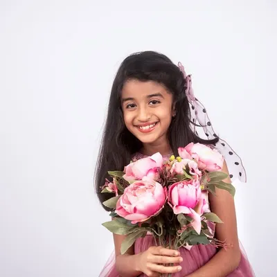 A beautiful studio portrait of a smiling girl holding a bouquet of pink flowers. The simple white background makes her joyful expression the star of the show.