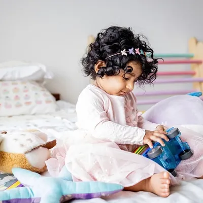 A quiet moment of play on the bed. This little girl is completely absorbed with her toy truck, surrounded by her other favorite stuffed animals. At-home sessions are perfect for capturing these authentic childhood moments.