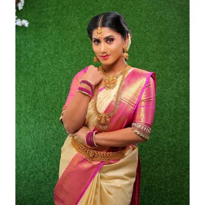 A classic South Indian look featuring a cream and pink silk saree. The makeup includes a warm, blended eyeshadow, defined brows, and a soft lip color to create an elegant and graceful appearance.