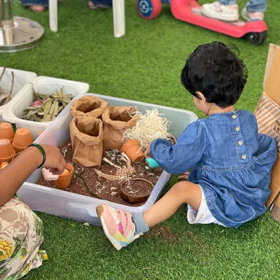 Our sensory play zones are a paradise for toddlers. This little one is exploring a gardening-themed sensory bin, a hands-on activity that is fantastic for developing fine motor skills and engaging their sense of touch.