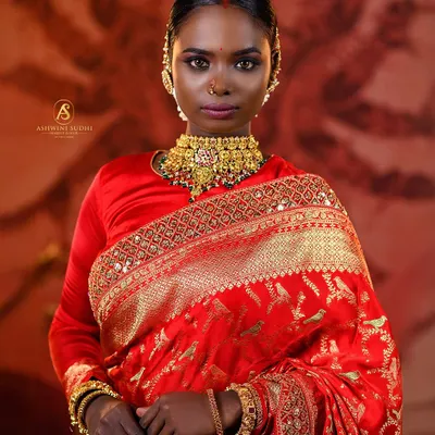 A powerful portrait of a South Indian bride in a classic red silk saree. The focus is on her confident gaze, the bold gold choker, and the traditional bindi, creating a look of pure regality.