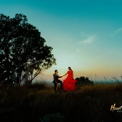 A breathtaking pre-wedding portrait on a hilltop at sunset. The flowing red gown against the twilight sky creates a truly cinematic feel for your love story.