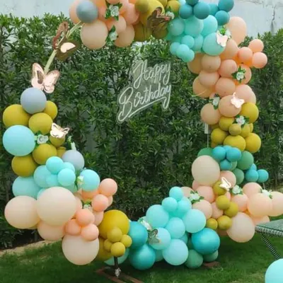 A beautiful pastel balloon ring set up in a garden. This outdoor decoration, adorned with delicate butterflies, creates a whimsical and enchanting photo backdrop, perfect for a daytime birthday party.