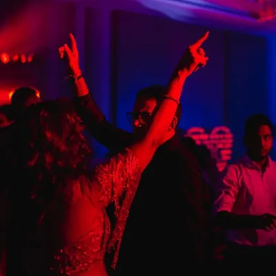 The energy of the sangeet dance floor captured with dramatic red and blue lighting. We use motion blur and creative lighting to convey the vibrant atmosphere of the party.