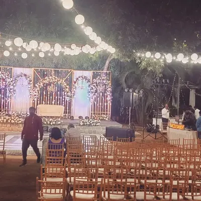 A wide view of an outdoor reception setup at night, featuring a beautifully lit stage and elegant guest seating under string lights.