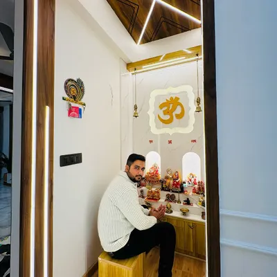 Sitting in a completed mandir at Prateek Laurel. This serene space features a backlit 'Om' symbol, a beautiful wooden ceiling design with profile lights, and ample space for prayer.