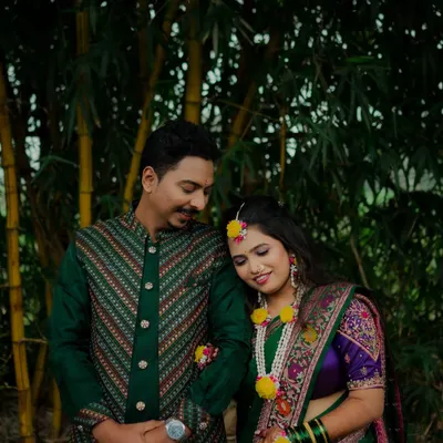 A sweet, candid moment during a Haldi photoshoot. The bride rests her head on the groom's shoulder, both adorned in floral jewelry, sharing a quiet moment before the festivities.