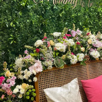 For this botanical garden baby shower, we created a lush greenery wall with a 'Mommy to be' sign. The seating area is adorned with an abundance of fresh, colorful flowers for a luxurious and natural feel.