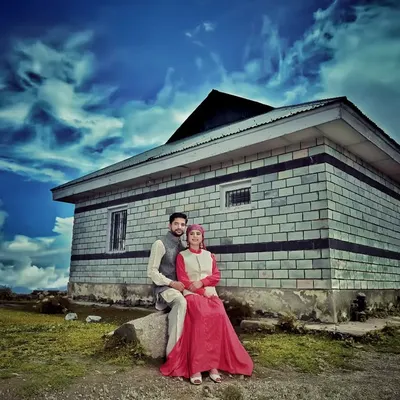 A dramatic pre-wedding portrait featuring a couple in front of a traditional stone house under a striking blue sky. This style of editing and composition creates a powerful, memorable image for your album.