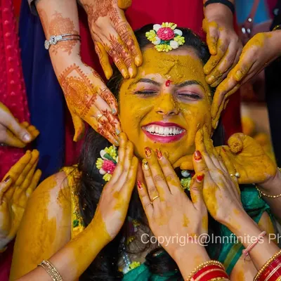 The Haldi ceremony is all about fun and family. This shot, with hands coming from all directions, perfectly captures the joyful chaos and the bride's radiant smile.