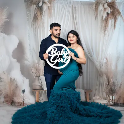 A couple's maternity portrait with the mother-to-be in a stunning teal gown, holding a 'Baby Girl' sign against a dreamy boho backdrop.