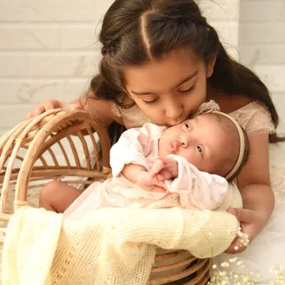 An incredibly sweet and gentle moment as an older sister gives her newborn sibling a soft kiss on the forehead. This close-up shot captures the pure love and tenderness between them.