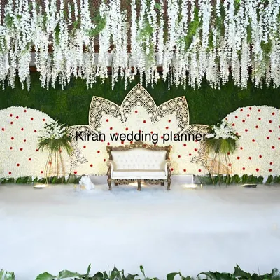 An elegant white floral reception stage featuring two large semi-circular backdrops and a central lotus motif. The addition of low-lying fog creates a dreamy, cloud-like effect for the couple.