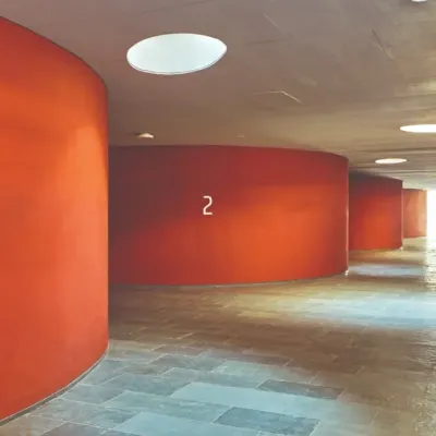 Circular skylights punctuate the ceiling of a corridor, casting pools of natural light onto the floor. This simple gesture transforms a simple circulation space into a dynamic experience, marked by a rhythm of light and dark.