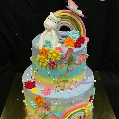 A magical two-tier unicorn cake for a 5th birthday. This 4kg Dutch Truffle cake is decorated with rainbows, colorful flowers, and a sleepy unicorn, all made with buttercream.