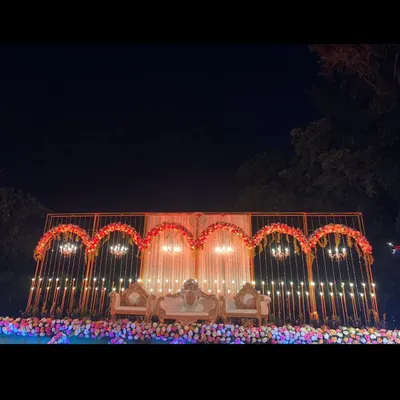 This wide view showcases a complete reception stage setup for a destination wedding in Lonavala. The design features a series of golden arches, elegant chandeliers, and a lush floral base, creating a grand and romantic backdrop for the couple.