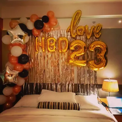 A classic bedroom birthday surprise for a partner, celebrating their 23rd birthday. This decoration features "HBD 23" and "love" foil balloons against a rose gold shimmer curtain, framed by a balloon arch in black, orange, and white.