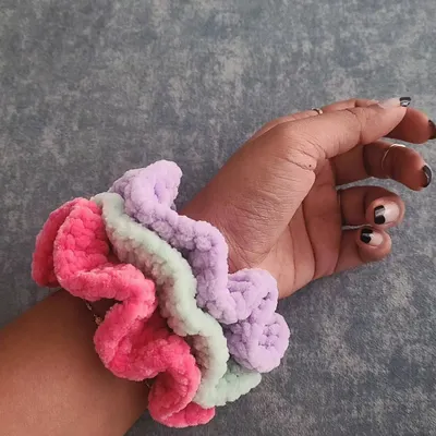 A stack of my fluffy velvet scrunchies worn on the wrist, showing off their fun colors. This set includes a vibrant pink, a soft mint green, and a lovely pastel purple. They are as much a cute accessory as they are a practical hair tie.