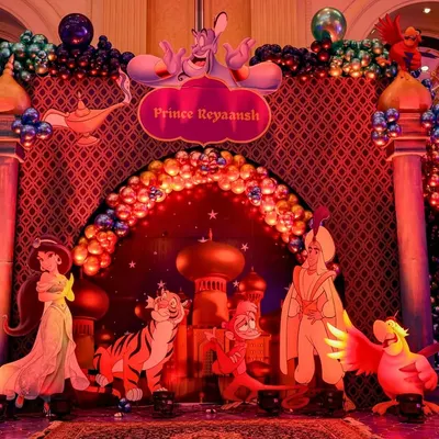 The main photo-op stage for this Aladdin-themed party, featuring a grand arch, a sparkling balloon arrangement, and cutouts of all the main characters.