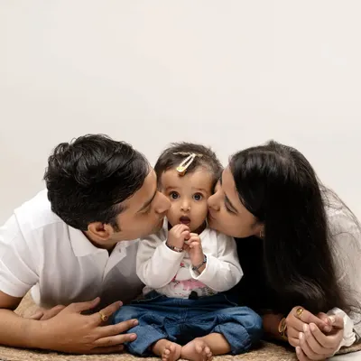 We believe in capturing pure love. This classic family portrait, with parents showering their little one with affection against a clean studio backdrop, is a timeless memory we love to create.